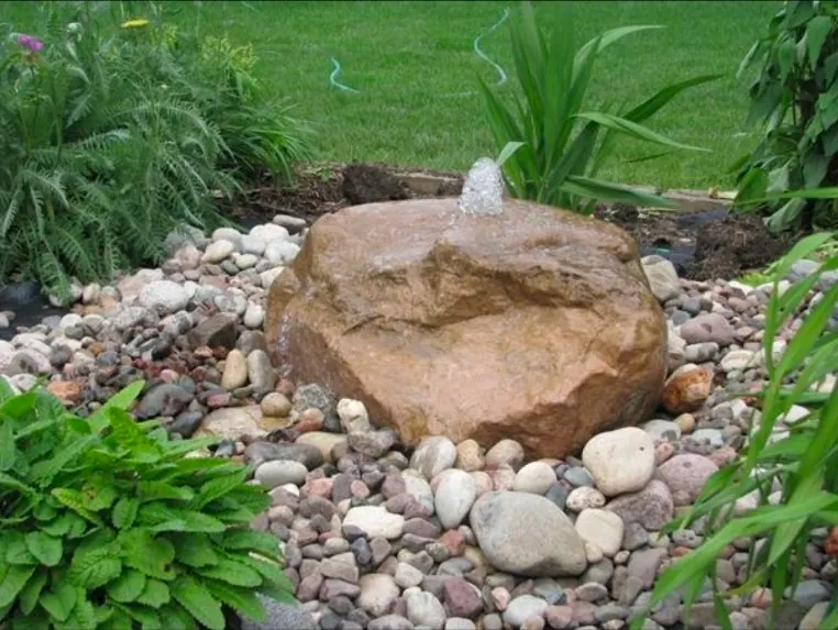 Bubbling boulder fountain surrounded by river rock and ferns