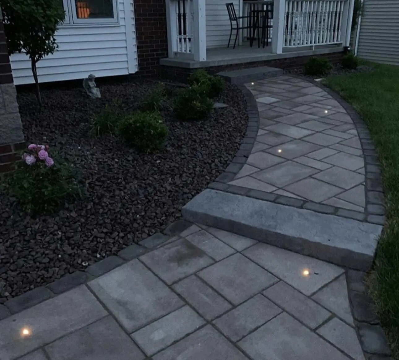 Curved paver walkway with in-ground lights and professional landscaping bed