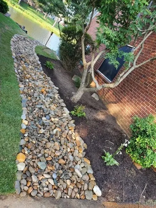 Decorative river rock drainage channel with mulch bed and tree