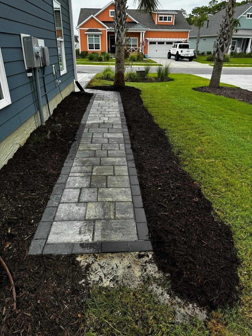 Gray paver walkway through mulch beds with palm trees in Florida neighborhood